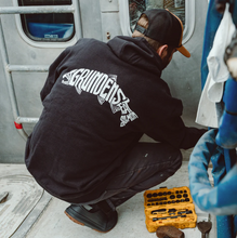 Load image into Gallery viewer, Person wearing a black hoodie with 'Grundéns' branding of the words grundens eat salmon on the shape of a fish, working on a boat.